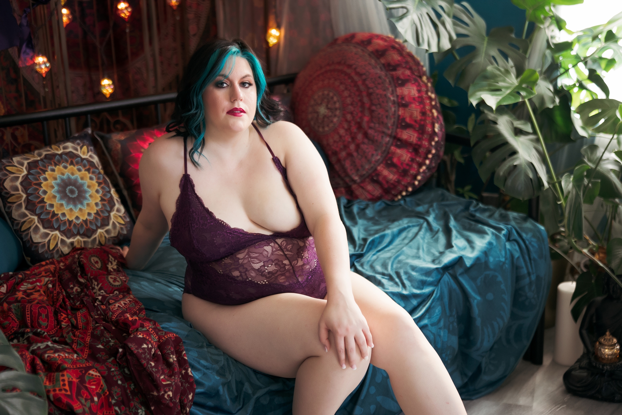 Miss M sits on a turquoise couch in front of colorful decorative pillows and plants in our Virginia Boudoir Studio